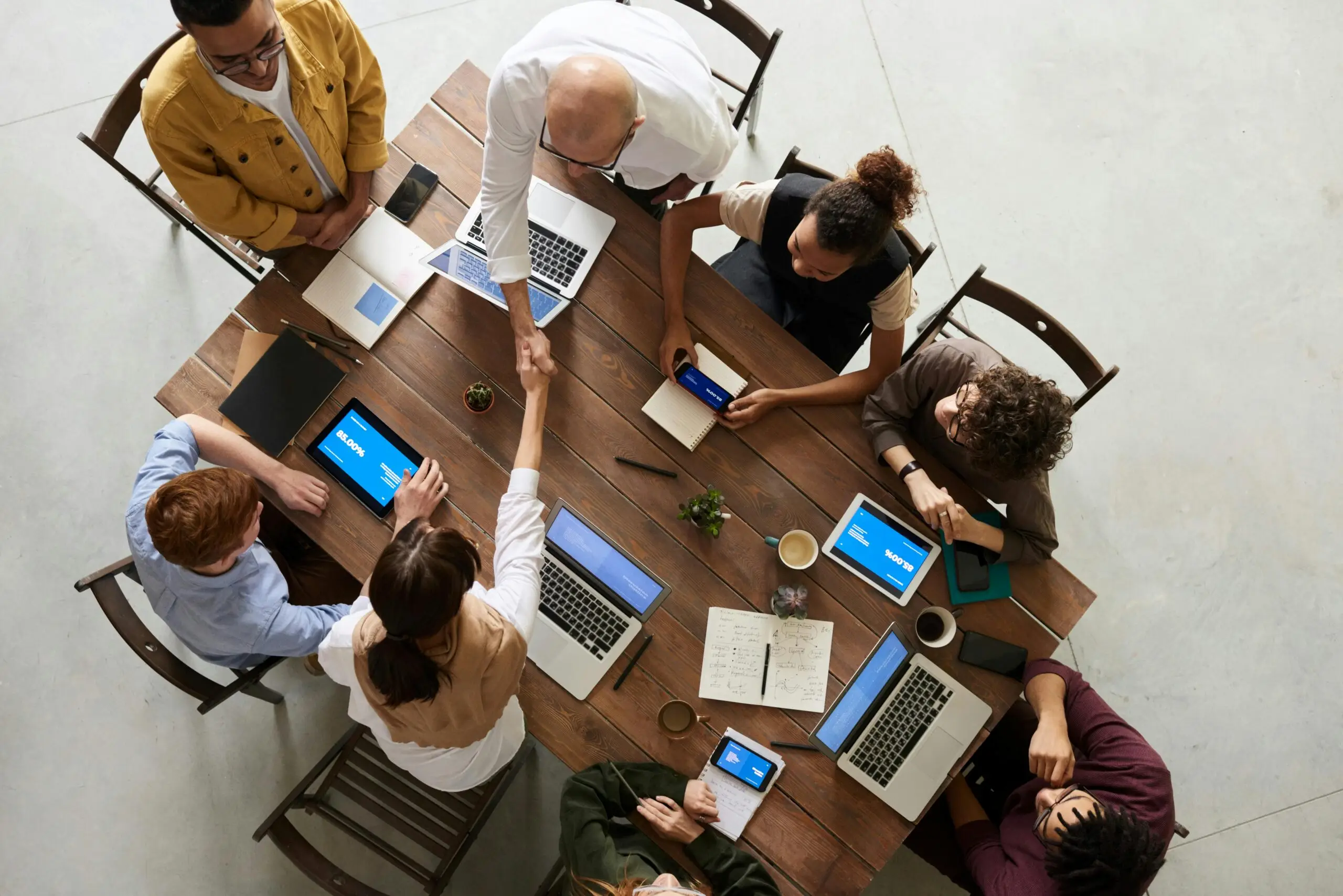 vista superior de un equipo diverso colaborando en un entorno de oficina con computadoras portátiles y tabletas, promoviendo la cooperación.
