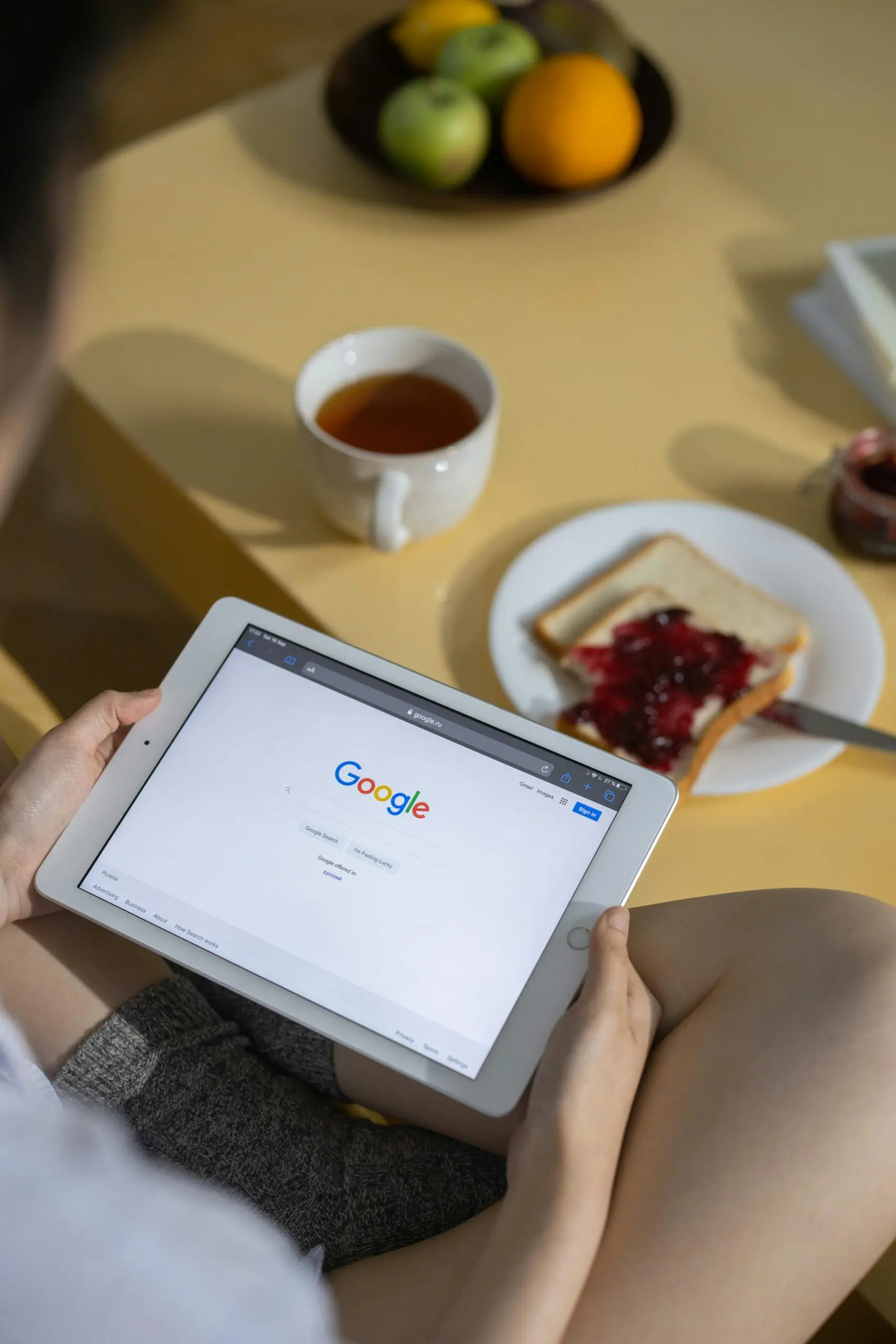 Persona que usa una tableta con la búsqueda de Google abierta mientras desayuna tostadas y té.