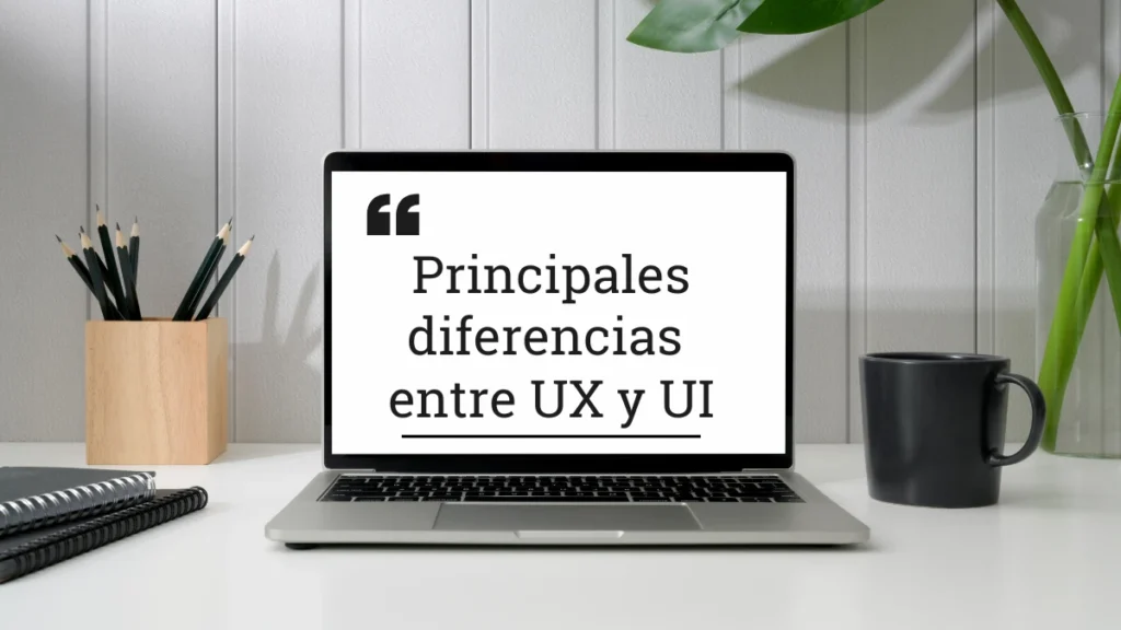 portátil sobre un escritorio minimalista, a su lado izquierdo un par de blocks de color negro y un portalápices con varios lápices de color negro en su interior, a una taza de color negro y un jarrón con plantas a su lado derecho, en su pantalla la frase "Principales diferencias entre UX y UI"